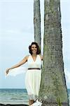 Woman in sundress at the beach, holding scarf in the breeze