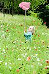 Little girl holding up butterfly net, standing in field of flowers