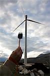 Man's Hand Holding Electric Plug by Wind Turbine