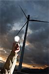 Man Holding Lightbulb by Wind Turbine