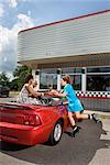 Waitress on Rollerskates Serving Food to Couple in Convertible at Drive-In Diner