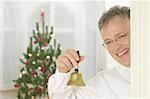 Man ringing a bell in front of a Christmas tree