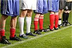 Six footballers in sports wear standing next to each other on a pitch whereas one of them is standing in the opposite direction (part of)