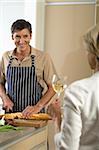 Mature man cutting baguette, woman drinking a glass of white wine