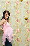 Pregnant woman in front of flowered wall, laughing at camera