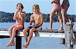 Two Boys with naked Torso eating Bread while two Girls in Bikini walk by - Snack - Leisure Time - Friendship - Lake