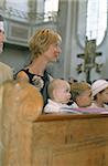 Blonde Woman and three little Children sitting on a Bench in a Church - Festivity - Faith - Christianity