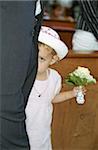 Little Girl in a white Dress with a Bunch of Flowers in her Hand hiding behind a Grown-Up - Bashfulness - Church - Celebration - Baptism - Christianity