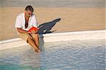 Man sitting at edge of pool and reading book