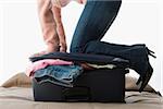 A woman kneeling on a suitcase full of clothes