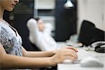 Woman typing on keyboard, colleague relaxing in background