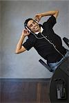 Young man leaning back in chair, listening to headphones