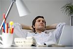 Man leaning back at desk with hands behind head