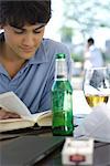 Junger Mann Buch zu lesen und mit einem Bier in einem Cafe im freien