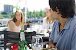 Young man sitting at outside cafe, looking over shoulder at young women sitting behind him