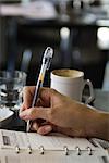 Woman sitting in cafe, writing in agenda, cropped view of hand