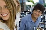 Young friends sitting at sidewalk cafe, looking over shoulders and smiling