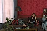 Frau sitzt auf dem Sofa, mit Handy und Betriebs-Dokument auf Runde