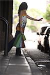 Young woman hailing taxi, carrying shopping bags