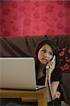 Woman using landline phone and laptop computer in living room, biting lip