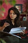 Woman sitting on sofa with document, looking down at cell phone