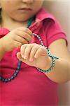 Little girl wrapping beaded necklace around wrist, cropped