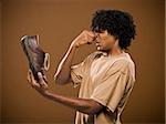 young man in a brown shirt holding a shoe and his nose.