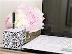 Laptop, Notizblock und Vase mit Blumen am Schreibtisch im Home Office