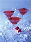 Three Cranberry Martinis and Red Christmas Ornaments on Snowy Background