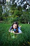 Girl Lying on Grass Looking at Jar of Fireflies