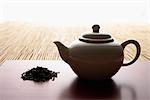 tea leaves in a pile and teapot on bamboo mat closeup