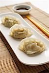 3 steamed gyoza dumplings placed on white plate with sauce on the side