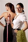 Chinese fashion designer measuring model's dress, smiling at camera