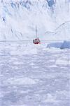 Red wooden boat crossing the ice in front of the Eqi Glacier, near Ilulissat, Greenland, Polar Regions