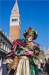 Person trägt maskiert Karneval Kostüm, St. Markusplatz und Campanile hinter der Karneval von Venedig, Venedig, Veneto, Italien