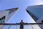 Un homme d'affaires en plein air avec les mains sur les rampes et les immeubles de bureaux modernes derrière