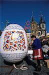A Moravian woman decorating a large egg with Easter designs on the Old Town Square, with Tyn Church in the background, Prague, Czech Republic, Europe