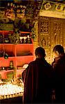 Mönche, die leichte butter Lampen in eine verheißungsvolle Nacht, beobachtet von zwei furchterregende Masken, Boudha Stupa Bodhnath, Kathmandu, Nepal.