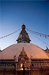 A monk lights butter lamps on gilded shrine at base of stupa at dawn, Swayambhunath (Swayambhu) (Monkey Temple) Buddhist stupa on a hill overlooking Kathmandu, UNESCO World Heritage Site, Nepal, Asia