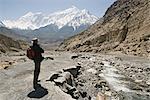 Trekker enjoys the view on the Annapurna circuit trek, Jomsom, Himalayas, Nepal. The high peak in the distance is 7021m Nilgiri, forming part of a wall known as The Grand Barrier.