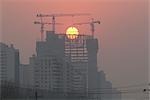 The sun sets behind cranes during the construction of the new Polly Plaza at Dongsishitiao in central Beijing.