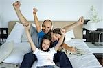 Family sitting together on bed with arms raised in air, all smiling