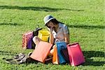 Young woman sitting in park, surrounded by shopping bags