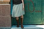 Young woman in trendy clothing leaning against wall, low section