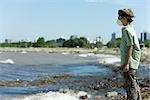 Boy wearing pollution mask, standing on polluted shore