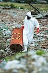 Person in protective suit carrying barrel of hazardous waste