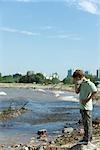 Boy standing on polluted shore, wearing pollution mask, head down