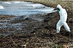 Person in protective suit walking along polluted shore