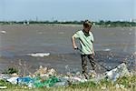 Boy picking up trash on polluted shore
