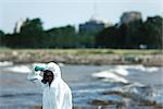 Person in protective suit looking at polluted water, side view